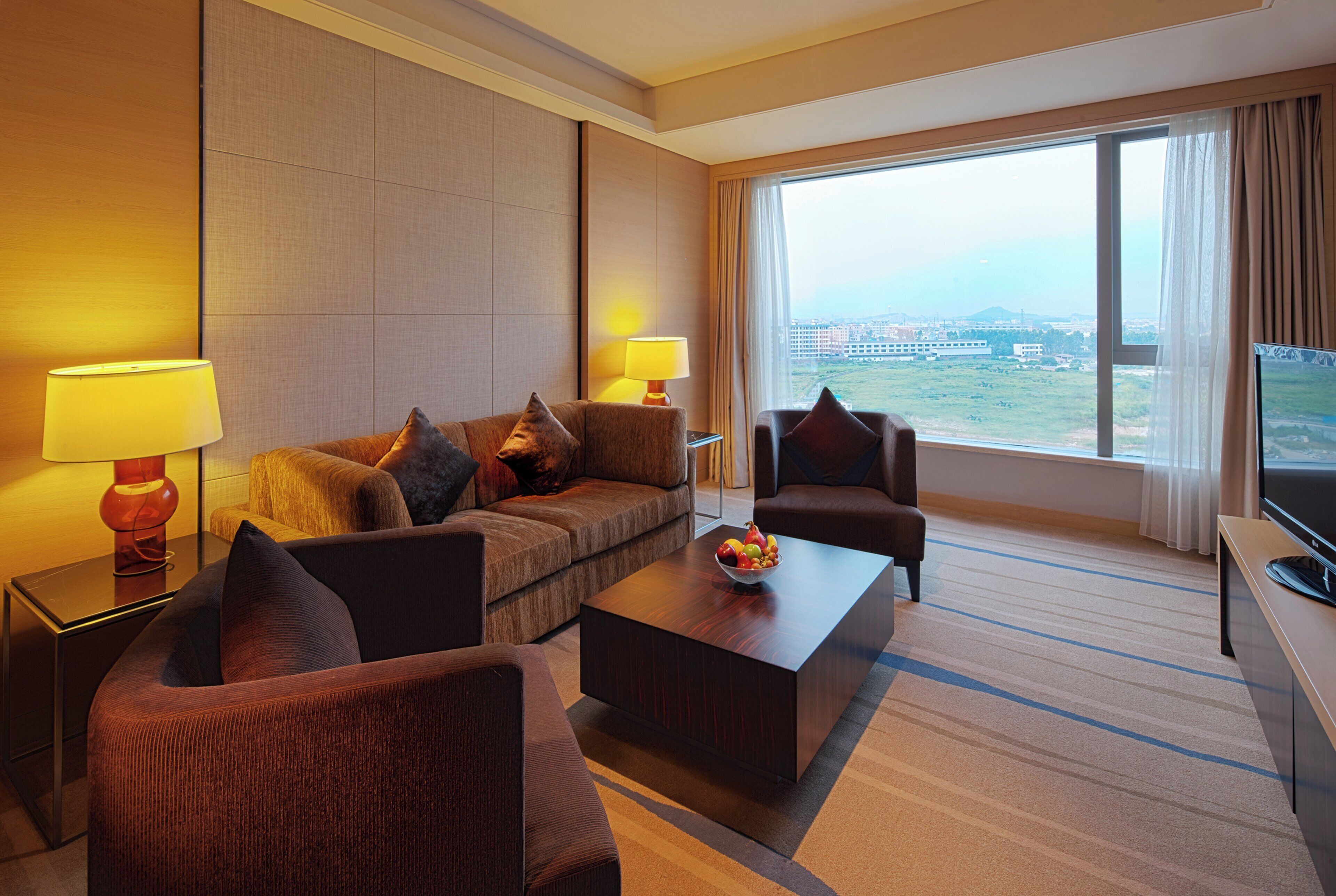 Una habitación de hotel con sofá, sillones, una mesita de centro y televisión.