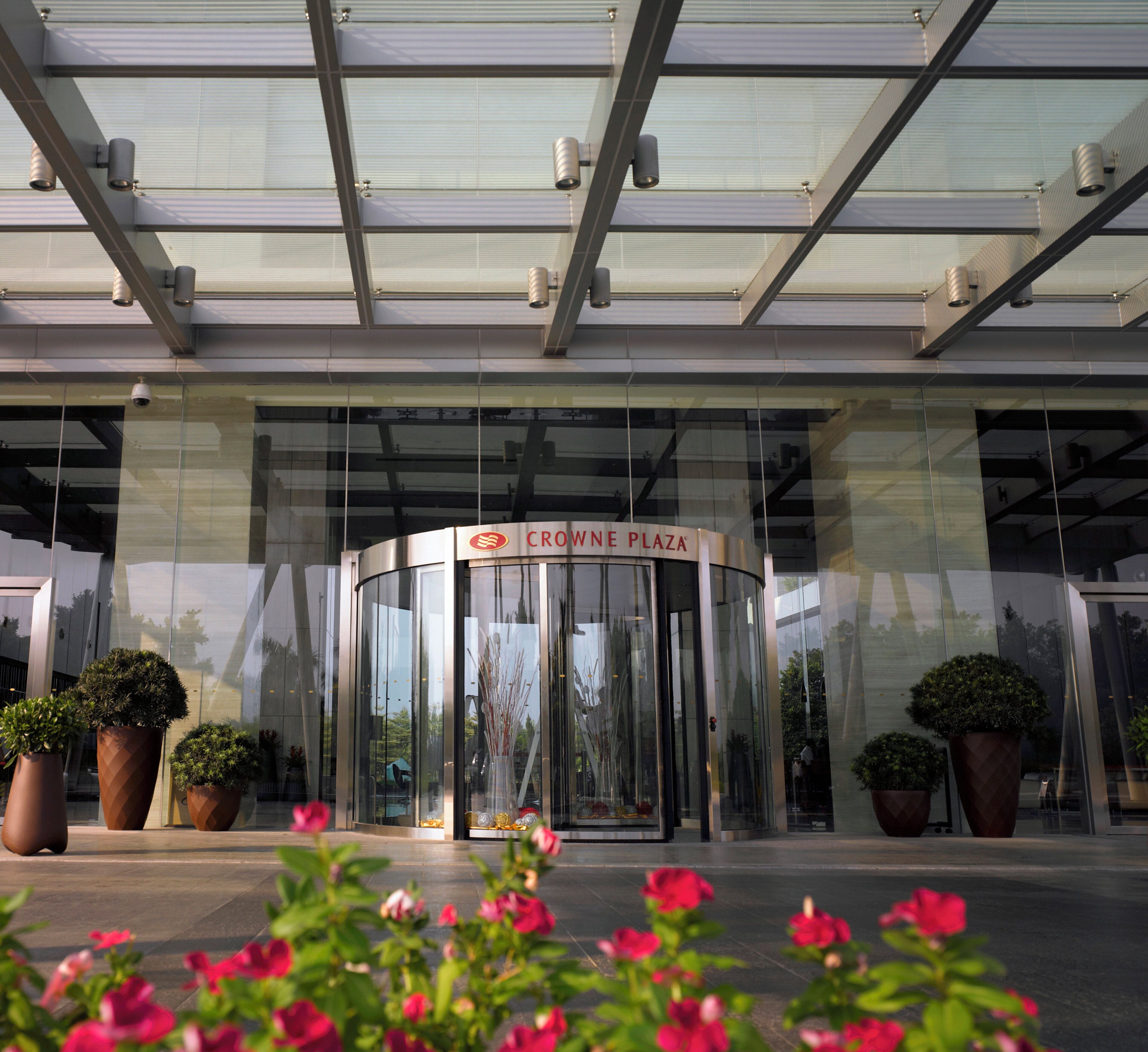 A modern building entrance with a revolving door and large potted plants.