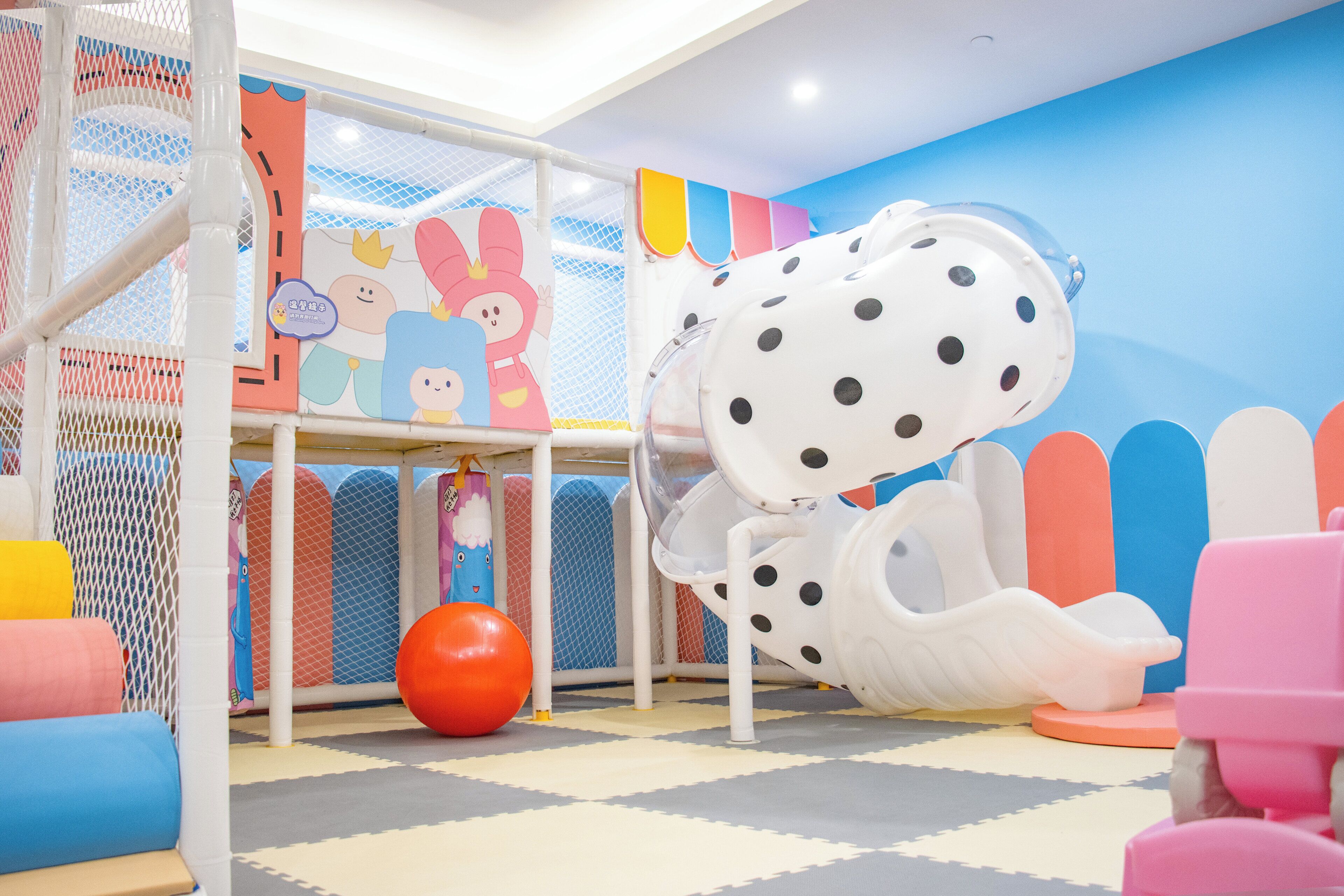A children's play area with a slide, soft play mats, and colorful decorations.