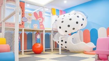 Zona de juegos infantiles con un tobogán, colchonetas blandas y decoraciones coloridas.