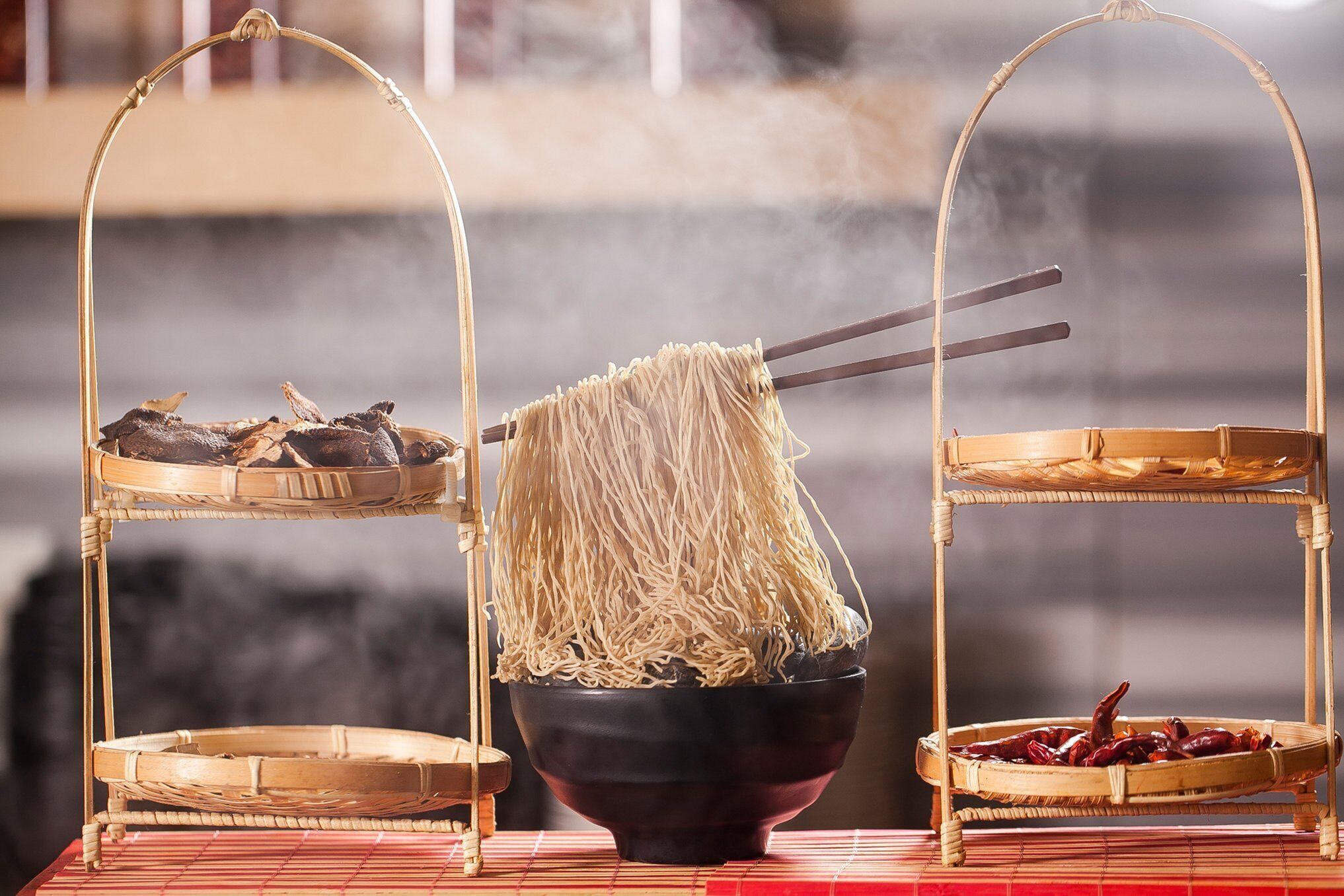 Una configuración tradicional china de hot pot con un tazón de fideos, carne seca y una cesta de dátiles rojos.
