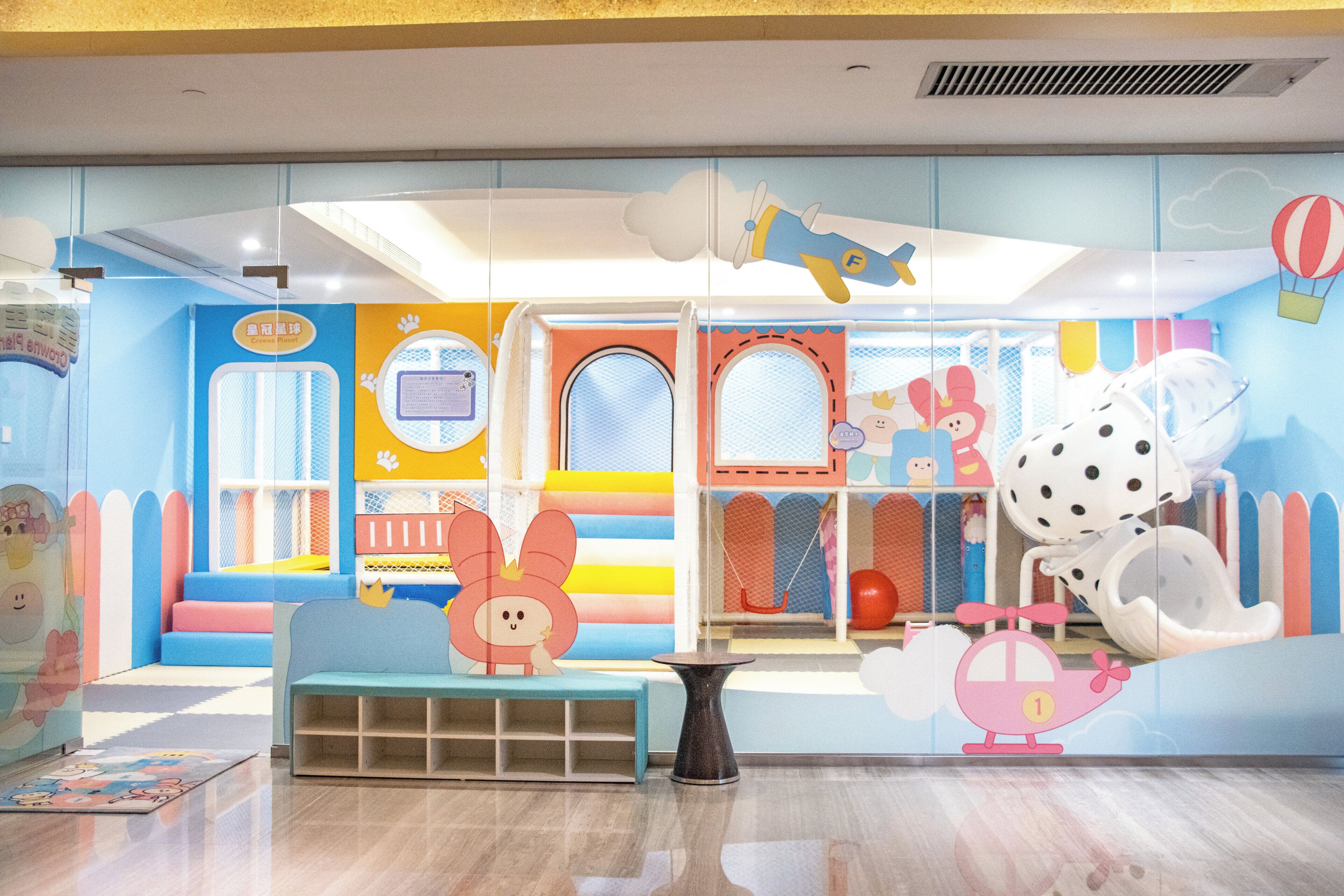 Een kleurrijk speelgebied voor kinderen, met een blauwe bank, een kleintje tafel en diverse speeltoestellen.