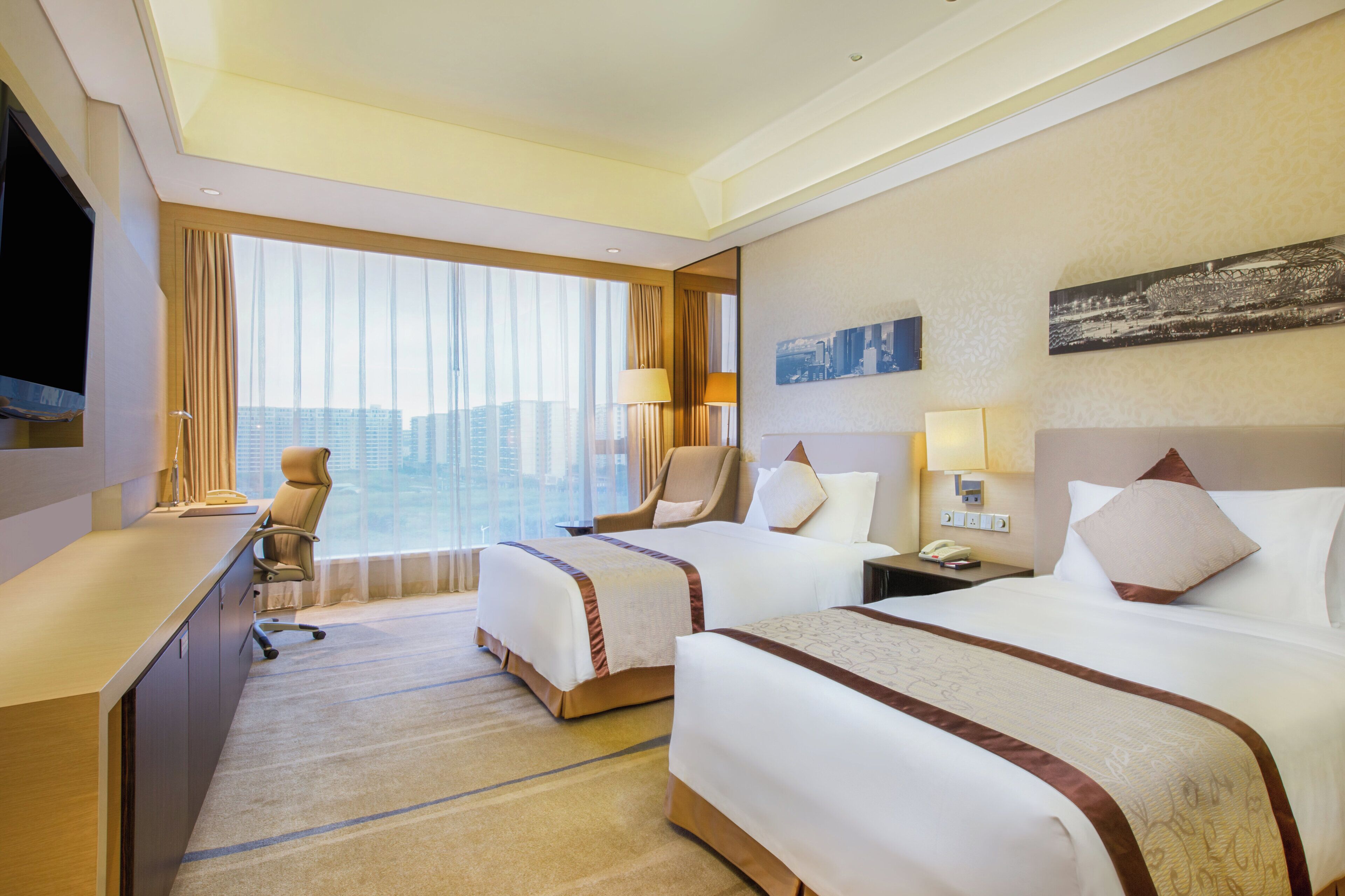 A hotel room with two beds, a desk, a chair, a TV, and a large window with curtains.