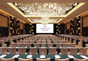 Een congreszaal met rijen tafels en stoelen, een grote kroonluchter en een scherm waarop de naam van het hotel staat.