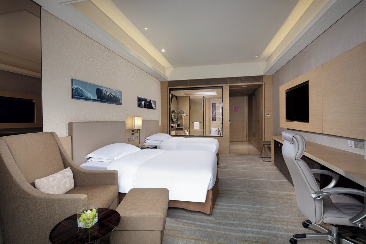 A hotel room with a large bed, two bedside tables, a sofa, a TV, and a mirror.
