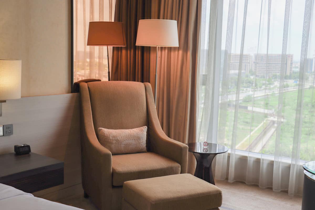 Une chambre d’hôtel avec une grande fenêtre, une chaise, une petite table et une lampe.