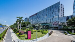 A modern building with a glass facade, a sign for Crowne Plaza, and a well-maintained landscaped area with palm trees and shrubs. - Crowne Plaza Guangzhou Huadu by IHG (Guangzhou)