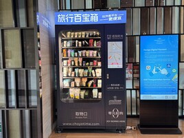Una macchina distributrice con diversi prodotti, uno schermo digitale informativo e un cartello con i dettagli di contatto.