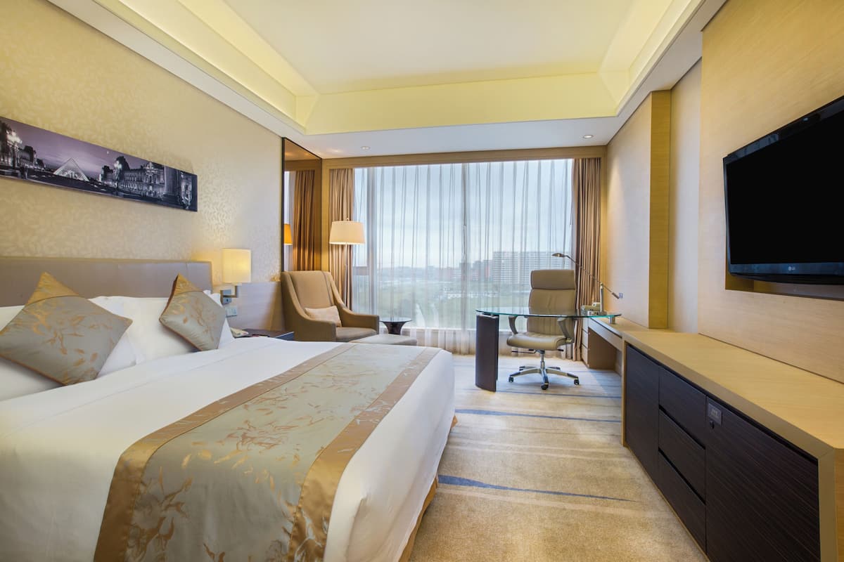 Une chambre d’hôtel avec un grand lit, un bureau, une chaise, une télévision et une vue sur la ville.