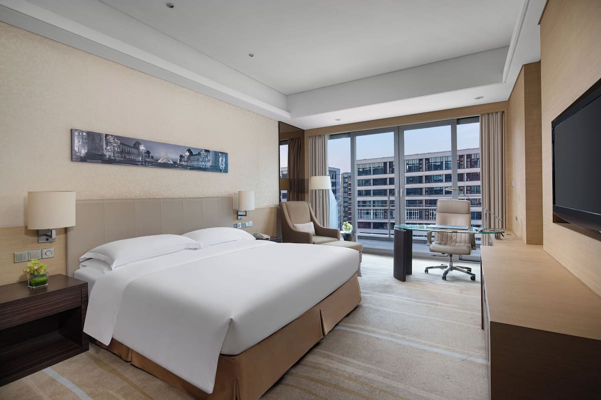 Une chambre d’hôtel avec un grand lit, un bureau, une chaise, une télévision et une fenêtre donnant sur la ville.