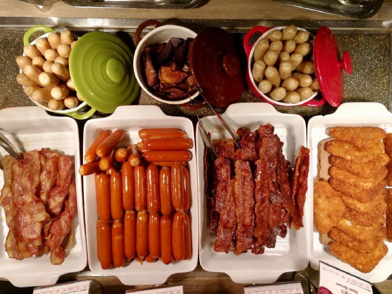 A buffet with various food items including sausages, bacon, and other meats.