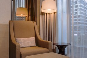 Een hotelkamer met een groot raam, een bank, een klein rond tafeltje en twee vloerlampen.
