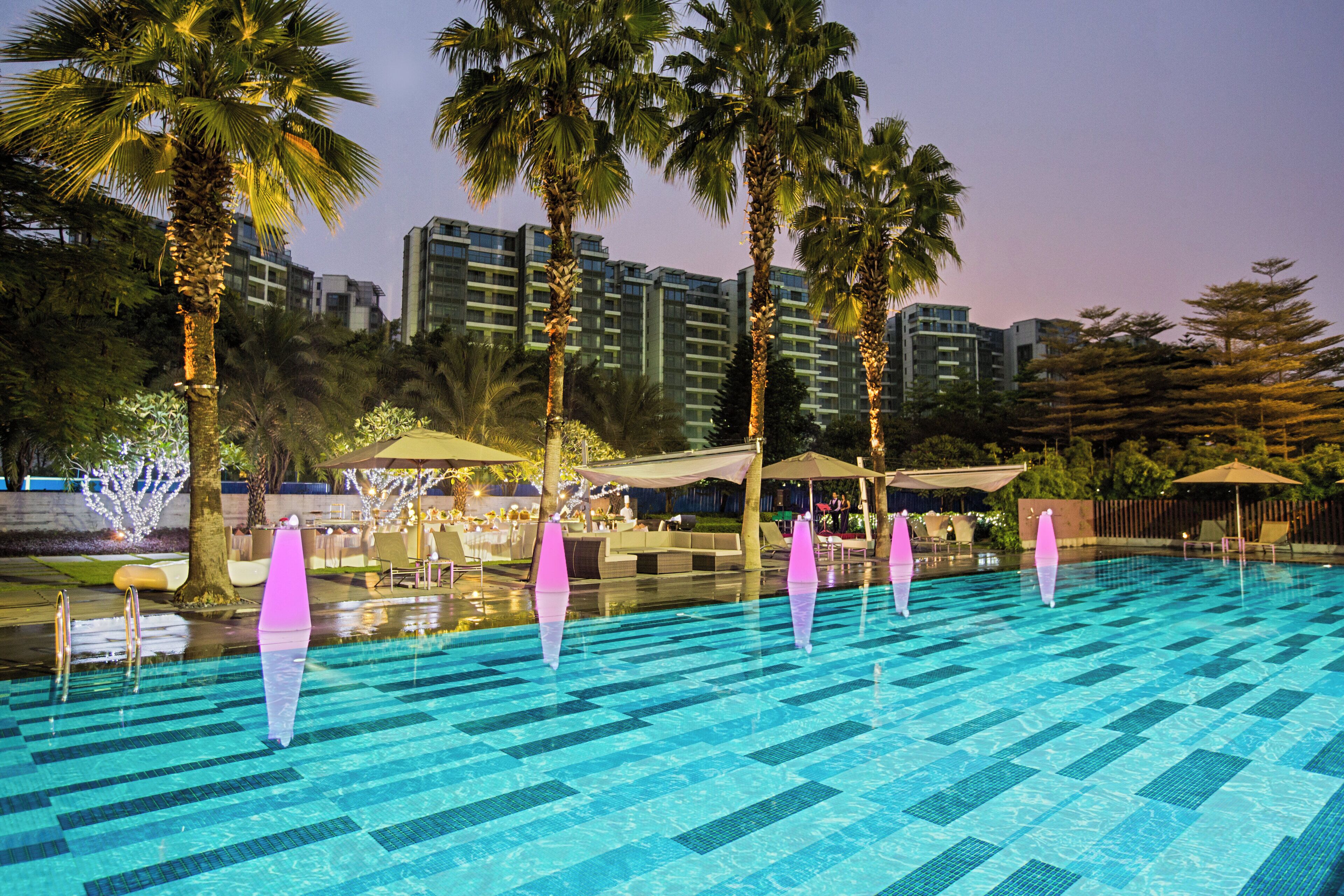 A swimming pool with clear blue tiles, surrounded by palm trees and outdoor seating areas.