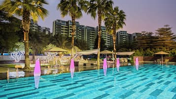 A swimming pool with clear blue tiles, surrounded by palm trees and outdoor seating areas.