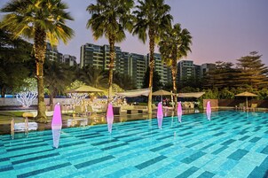 Una piscina con baldosas azules brillantes, rodeada de palmeras y zonas de estar al aire libre.