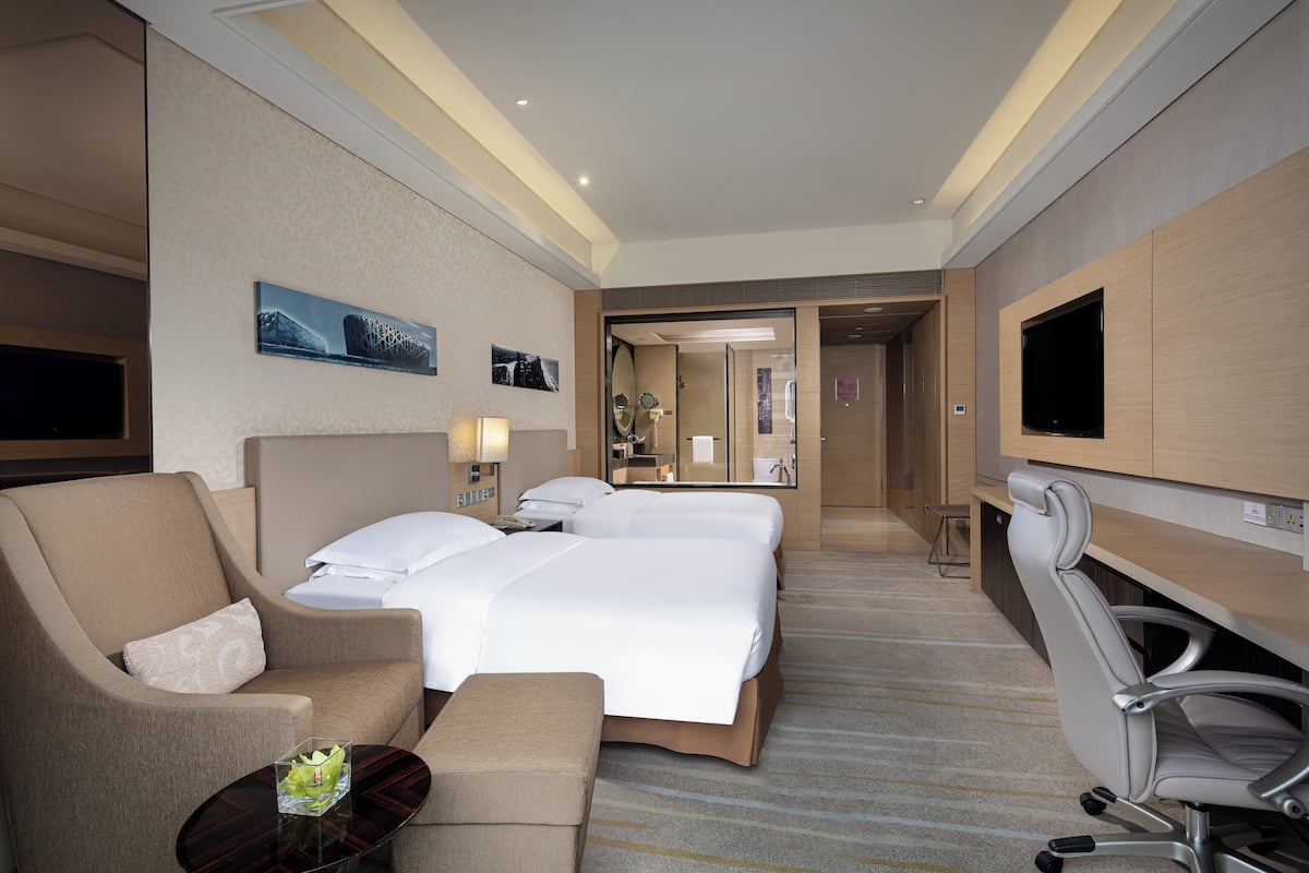 A hotel room with a large bed, two bedside tables, a sofa, a TV, and a mirror.