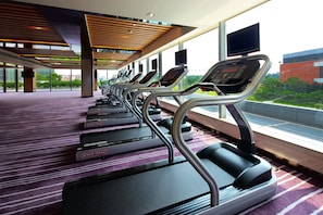 A row of treadmills in a modern indoor setting with large windows and a view of greenery outside.