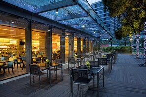 Un espace de restauration en plein air avec des tables et des chaises, une structure vitrée et des guirlandes lumineuses.
