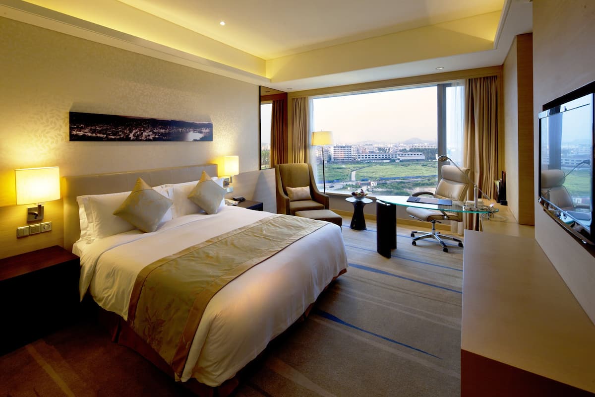 Une chambre d’hôtel avec un grand lit, un bureau, une chaise et une vue sur la ville.