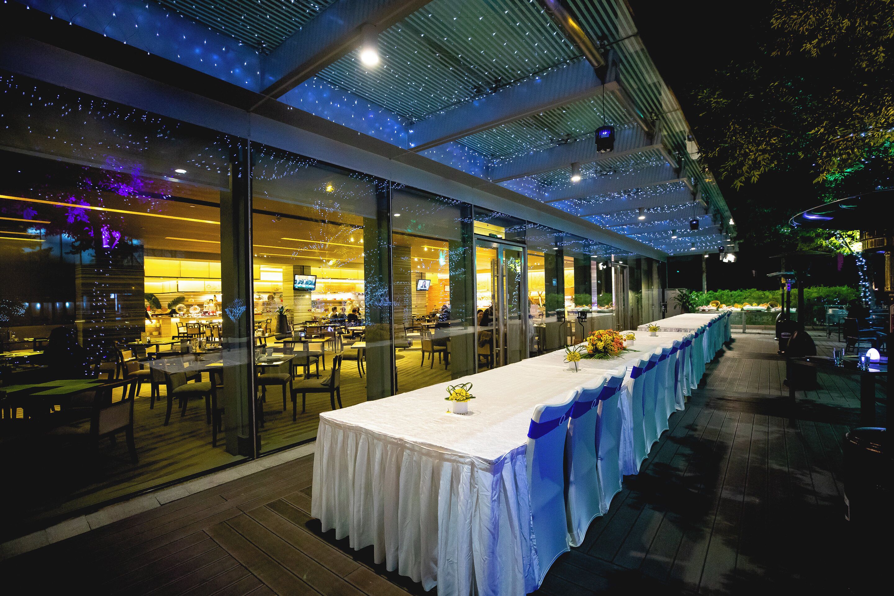 A restaurant with a long dining table, glass partitions, and a ceiling with string lights.