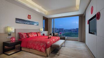 A hotel room with a large bed, bedside tables, a TV, and a view of the city.