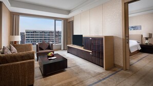 Een hotelkamer met een bank, een salontafel, een televisie, een kledingkast, een bed en uitzicht op de stad.