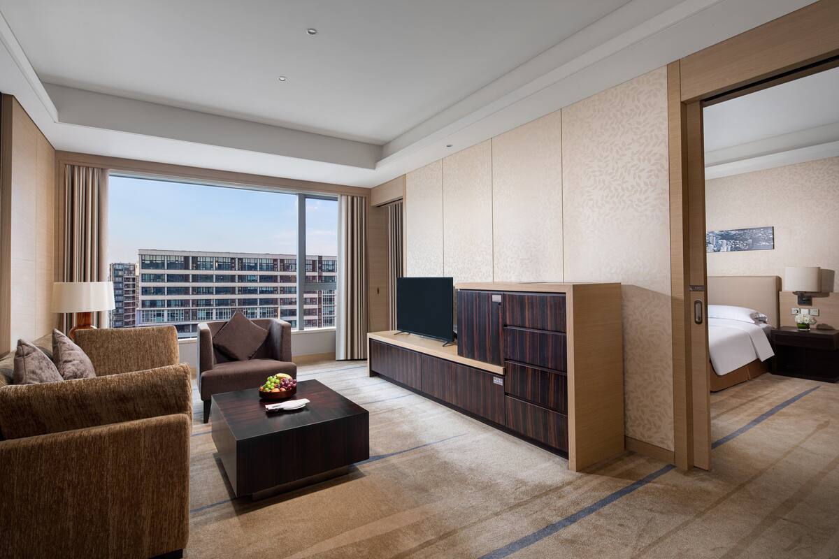 Une chambre d’hôtel équipée d’un canapé, d’une table basse, d’une télévision, d’une armoire, d’un lit et offrant une vue sur le paysage urbain.