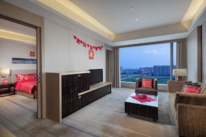 Quarto de hotel moderno com uma cama grande, televisão, sofá e vista para a paisagem urbana.