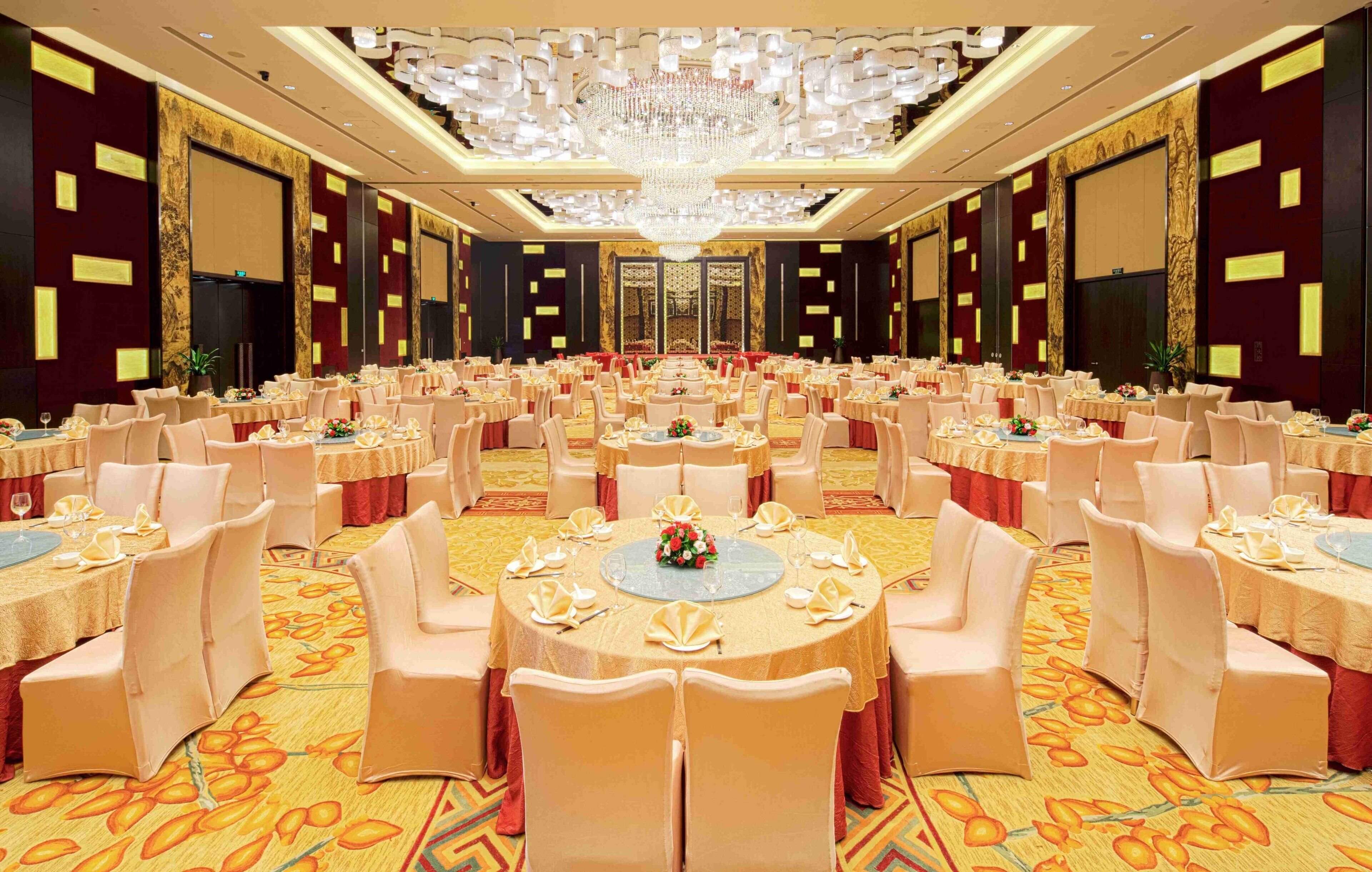 A large banquet hall with round tables, chairs, and a central chandelier.