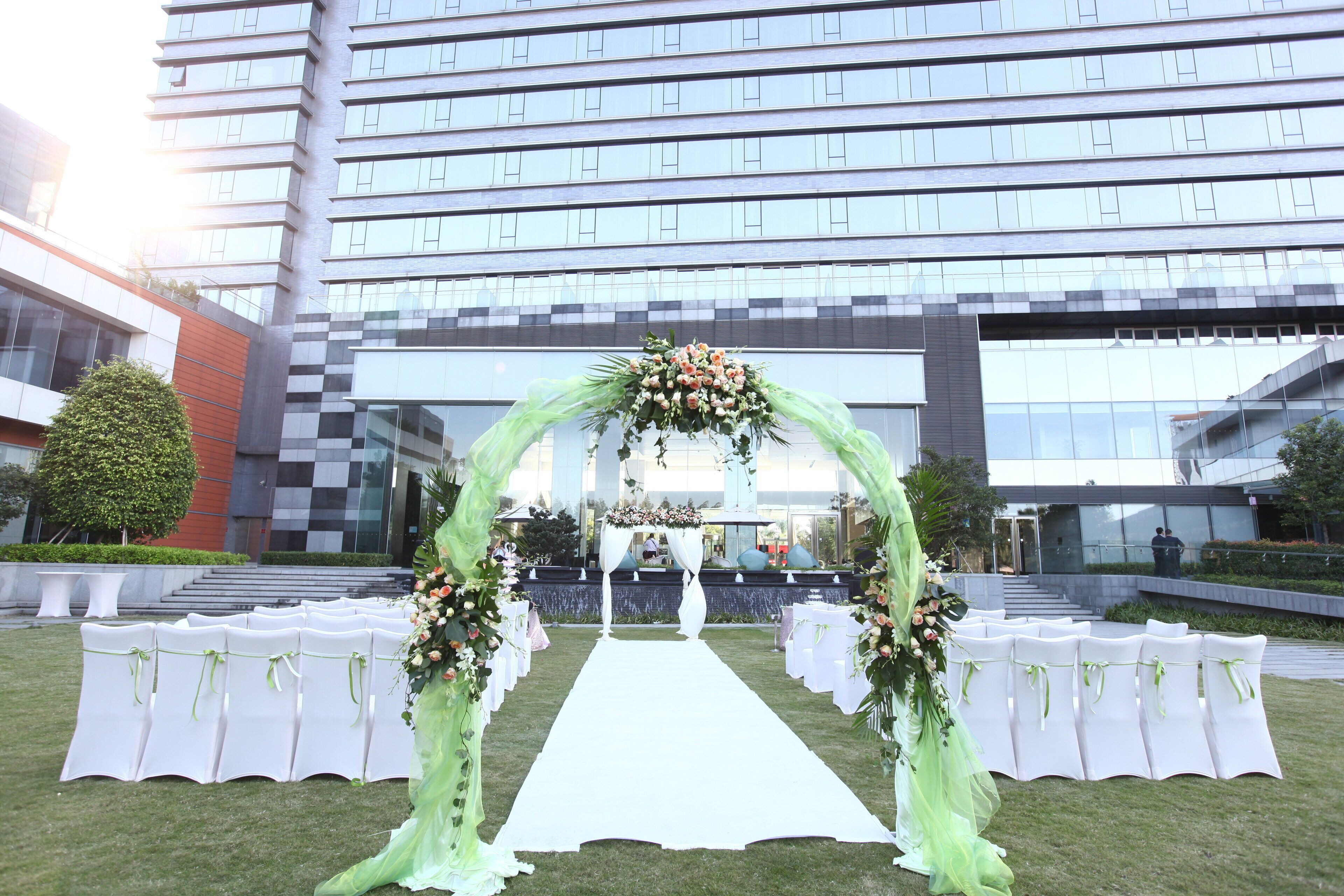 Decoración para boda al aire libre con un pasillo blanco, adornos florales y sillas blancas a cada lado.