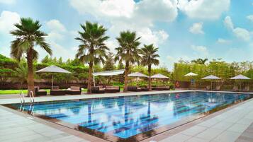 A swimming pool with lounge chairs and umbrellas, surrounded by palm trees and a clear sky.