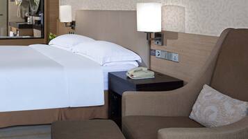 A hotel room with a bed, a sofa, a coffee table, a side table with a lamp, and a wall-mounted painting.