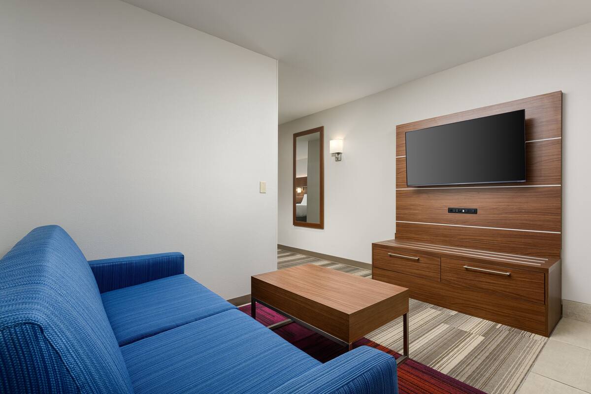Ein modernes Wohnzimmer mit einem blauen Sofa, einem Holztisch und einem an einer Holzkommode befestigten Fernseher.