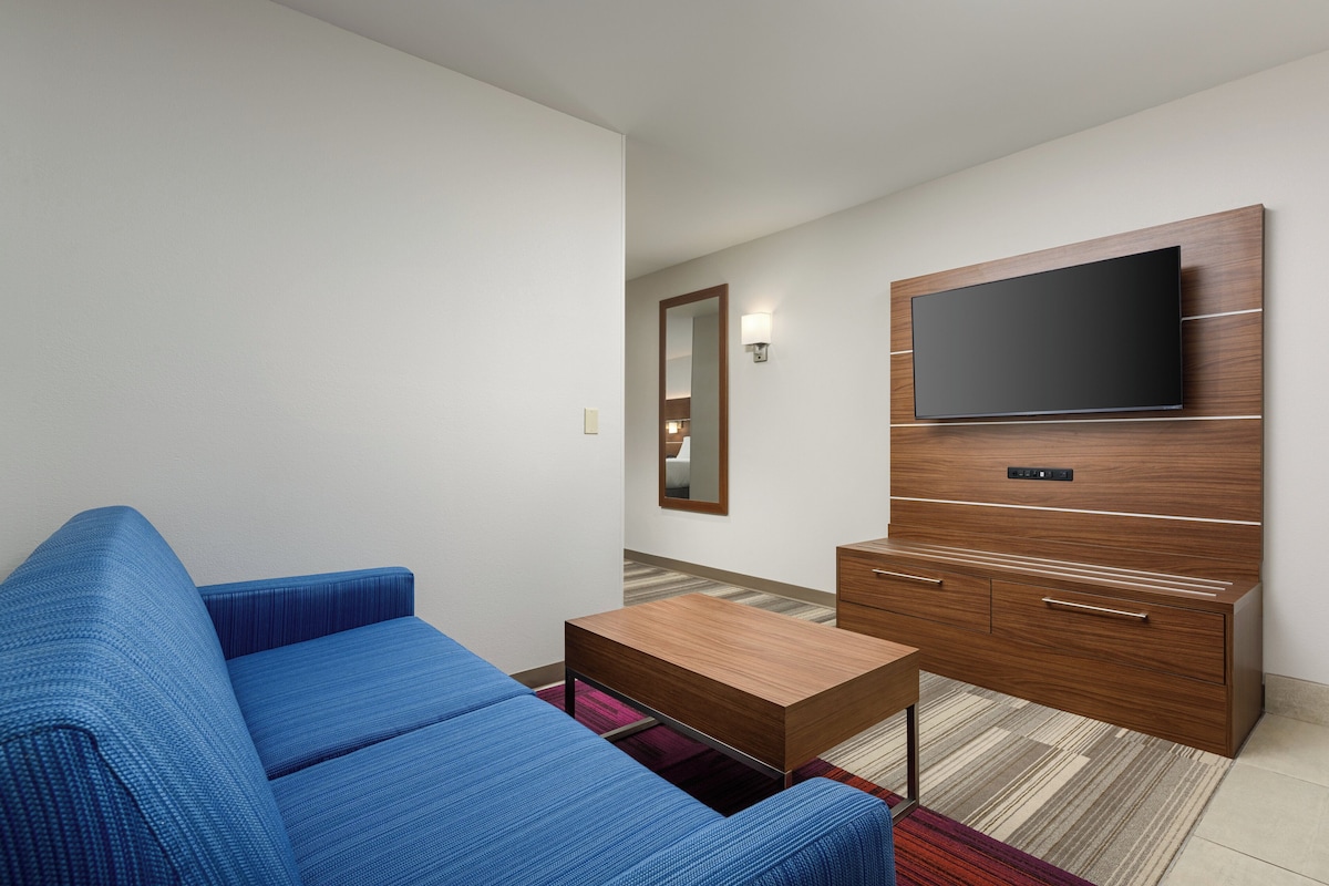 A modern living room with a blue sofa, a wooden coffee table, and a TV mounted on a wooden cabinet.
