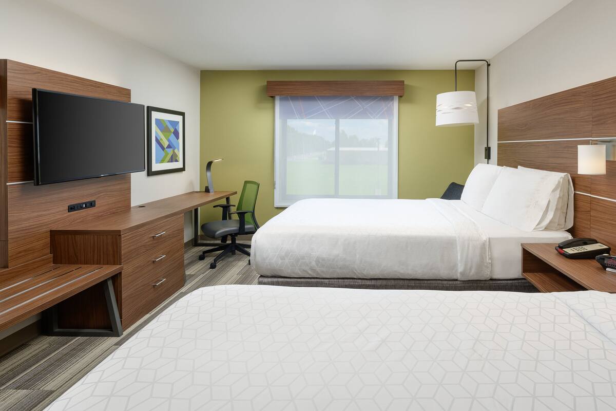 Ein Hotelzimmer mit Bett, Schreibtisch, Sessel, Fernseher und Fenster mit Ausblick ins Freie.