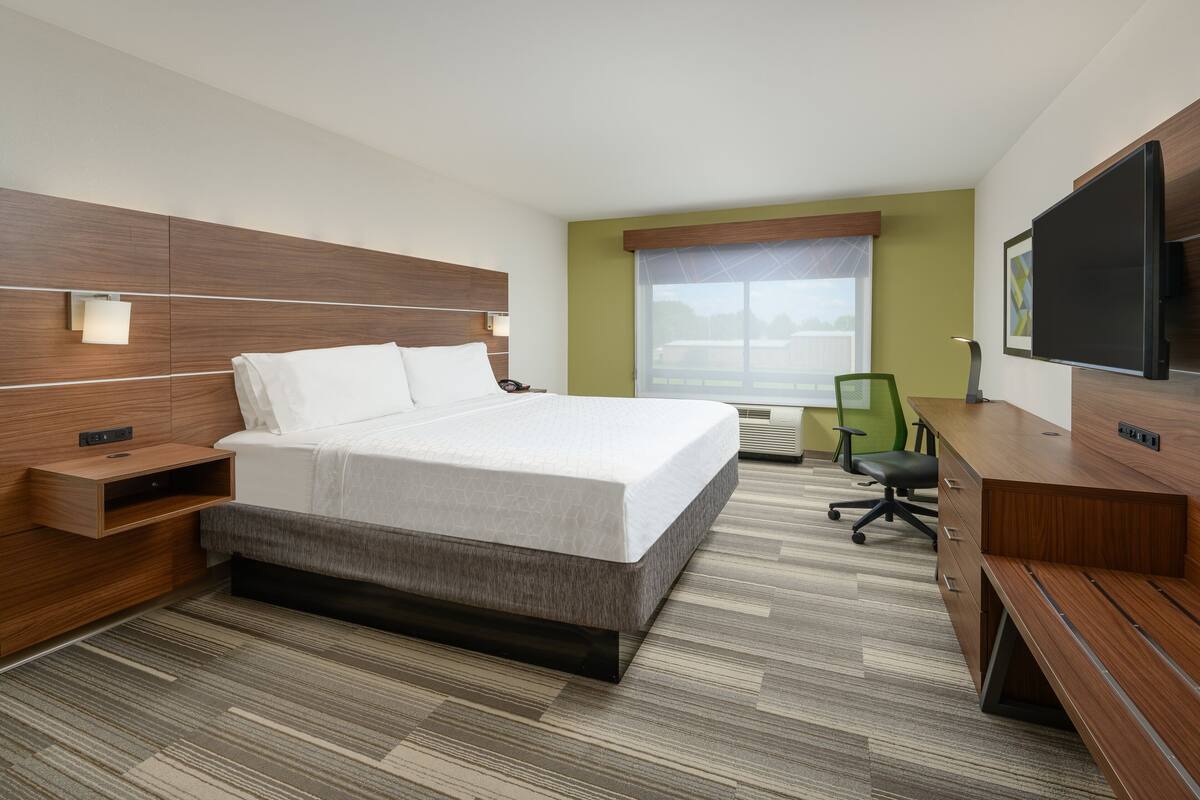 Ein Hotelzimmer mit Bett, Nachttisch, Schreibtisch, Stuhl, Fernseher und Fenster.