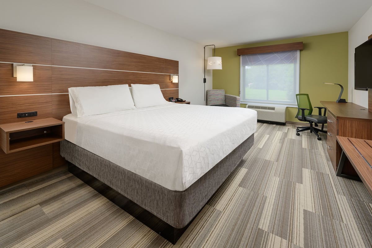 Ein modernes Hotelzimmer mit einem großen Bett, einem Schreibtisch, einem Sessel und einem Fernseher.