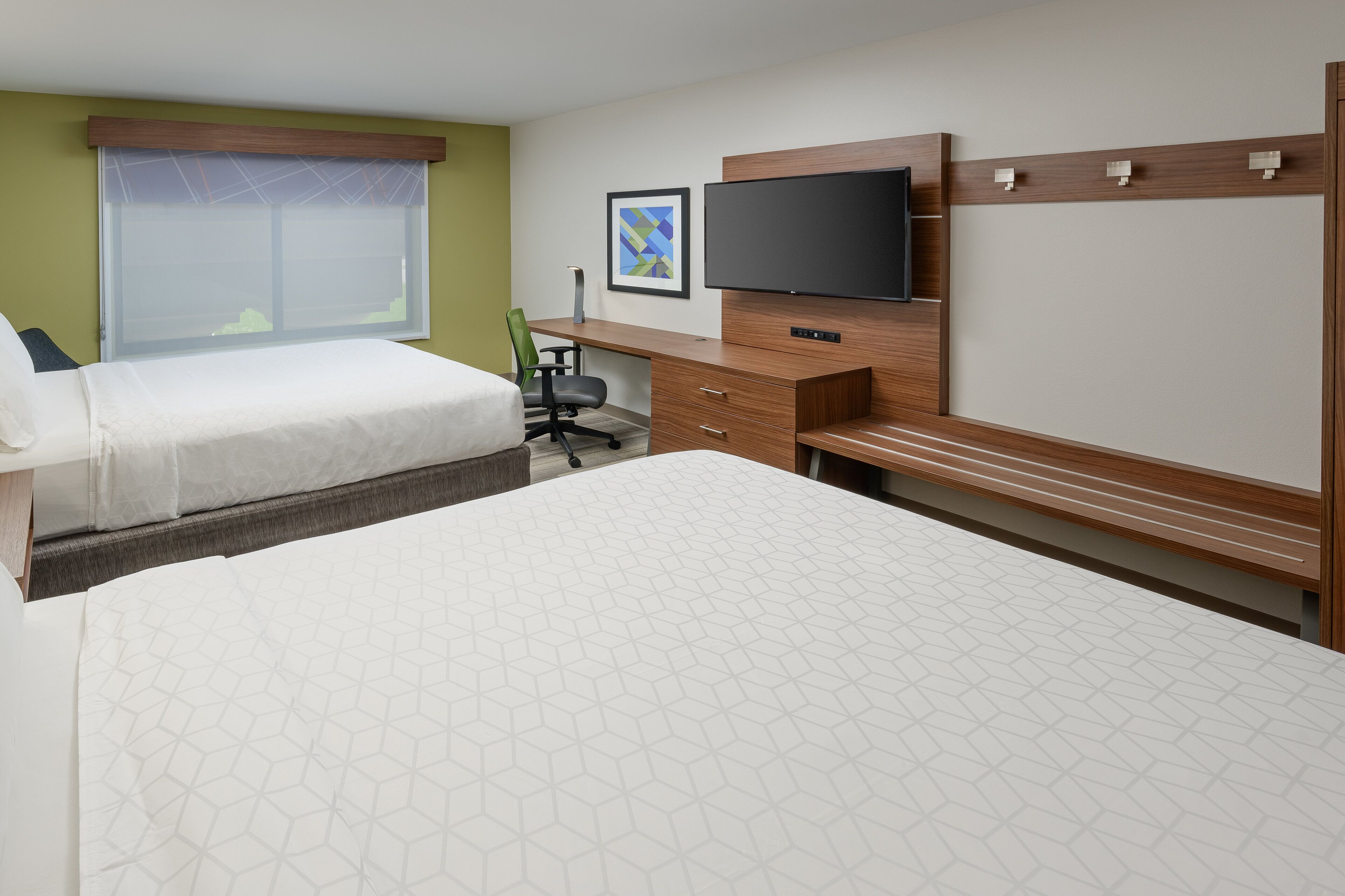A hotel room with two beds, a desk, a chair, a television, and a window with blinds.