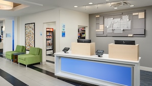 A hotel reception area with a counter, two green chairs, a refrigerator, and a wall-mounted display. - Holiday Inn Express Hotel & Suites Tullahoma by IHG (Tullahoma)