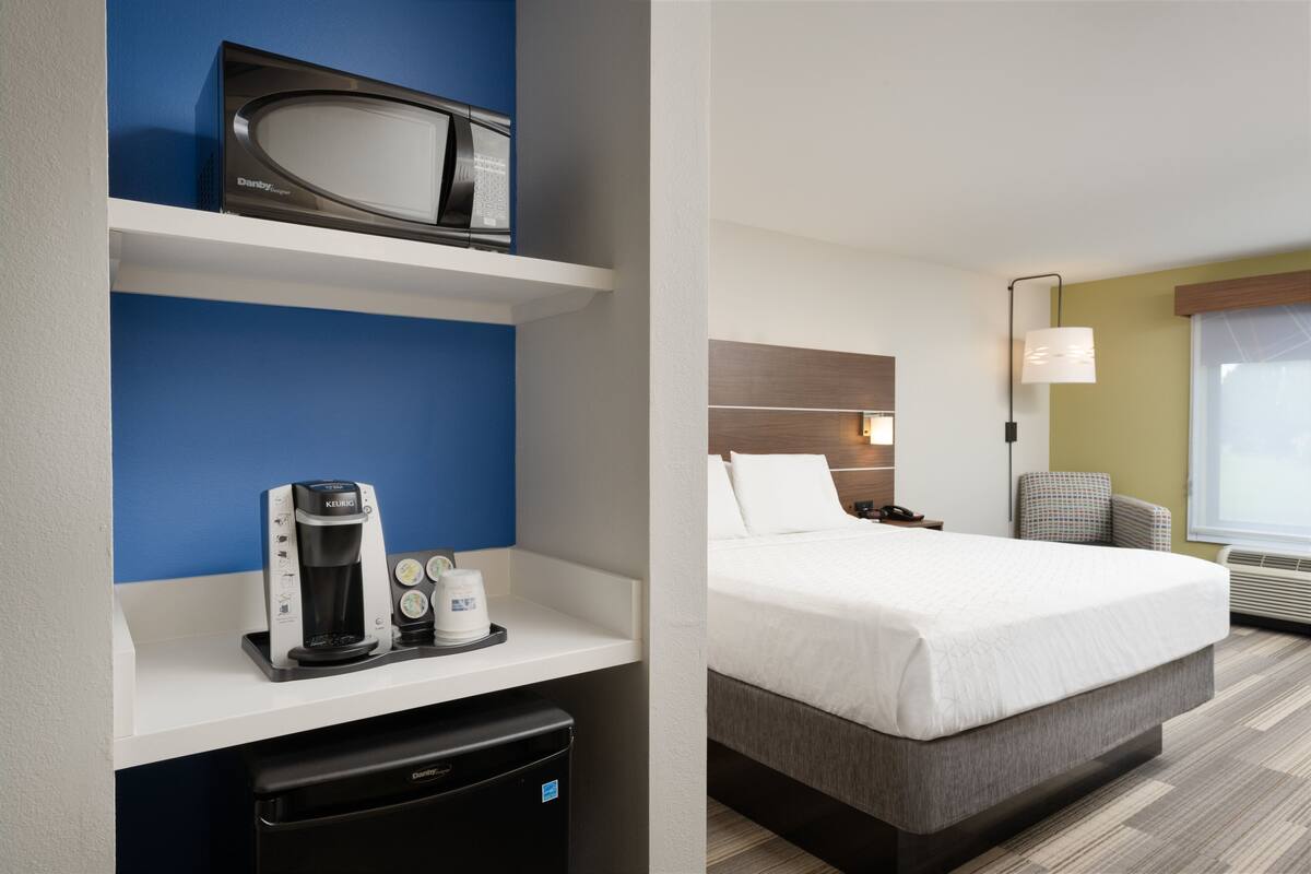 Ein Hotelzimmer mit Bett, Schreibtisch, Kaffeemaschine, Mikrowelle und kleinem Kühlschrank.