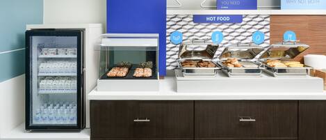 Un buffet du petit-déjeuner comprenant un présentoir réfrigéré pour les yaourts, un espace dédié aux plats chauds, et un panneau indiquant la disponibilité d’options à la fois saines et consistantes.