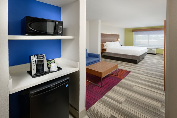 A hotel room with a bed, a microwave, a coffee maker, and a small refrigerator.