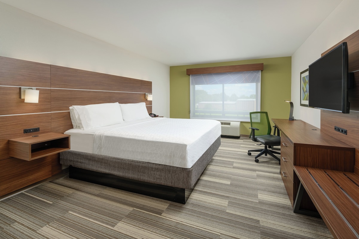 A hotel room with a bed, bedside table, desk, chair, TV, and window.