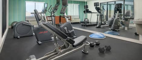 Un gimnasio con máquinas de cardio, mancuernas y un espejo grande.