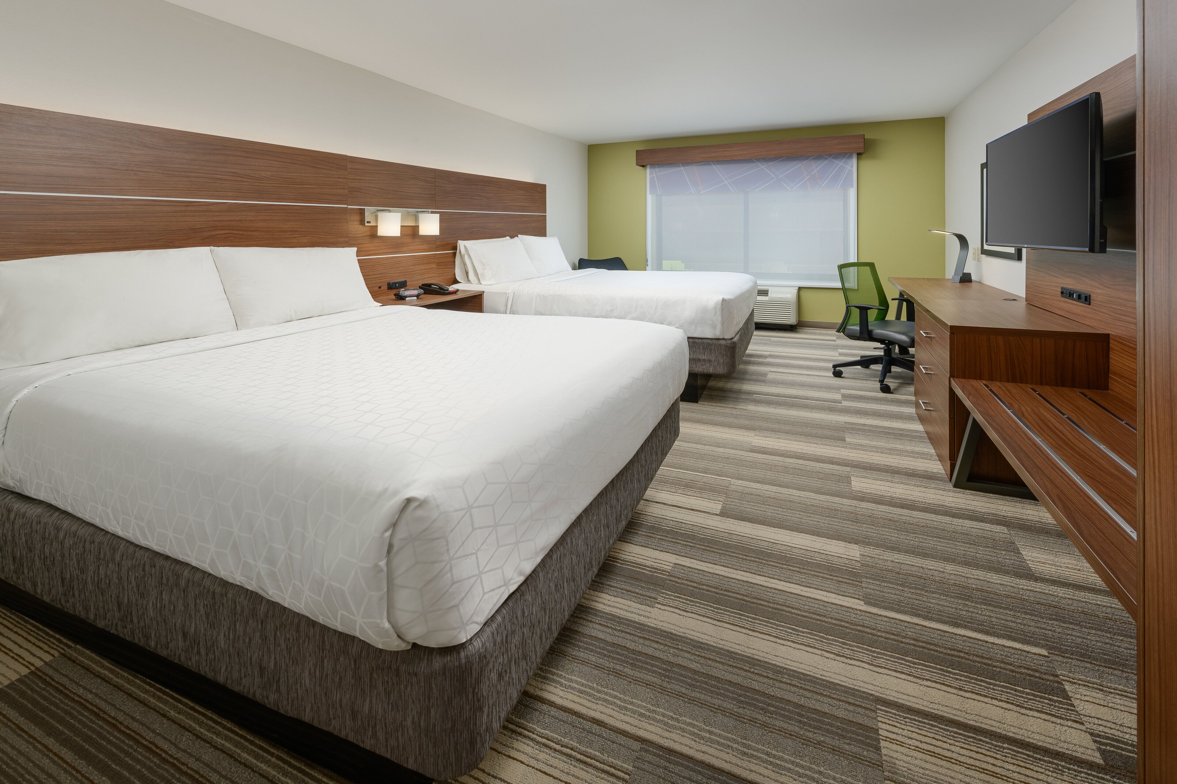 A hotel room with two beds, a desk, a chair, a television, and a window with blinds.