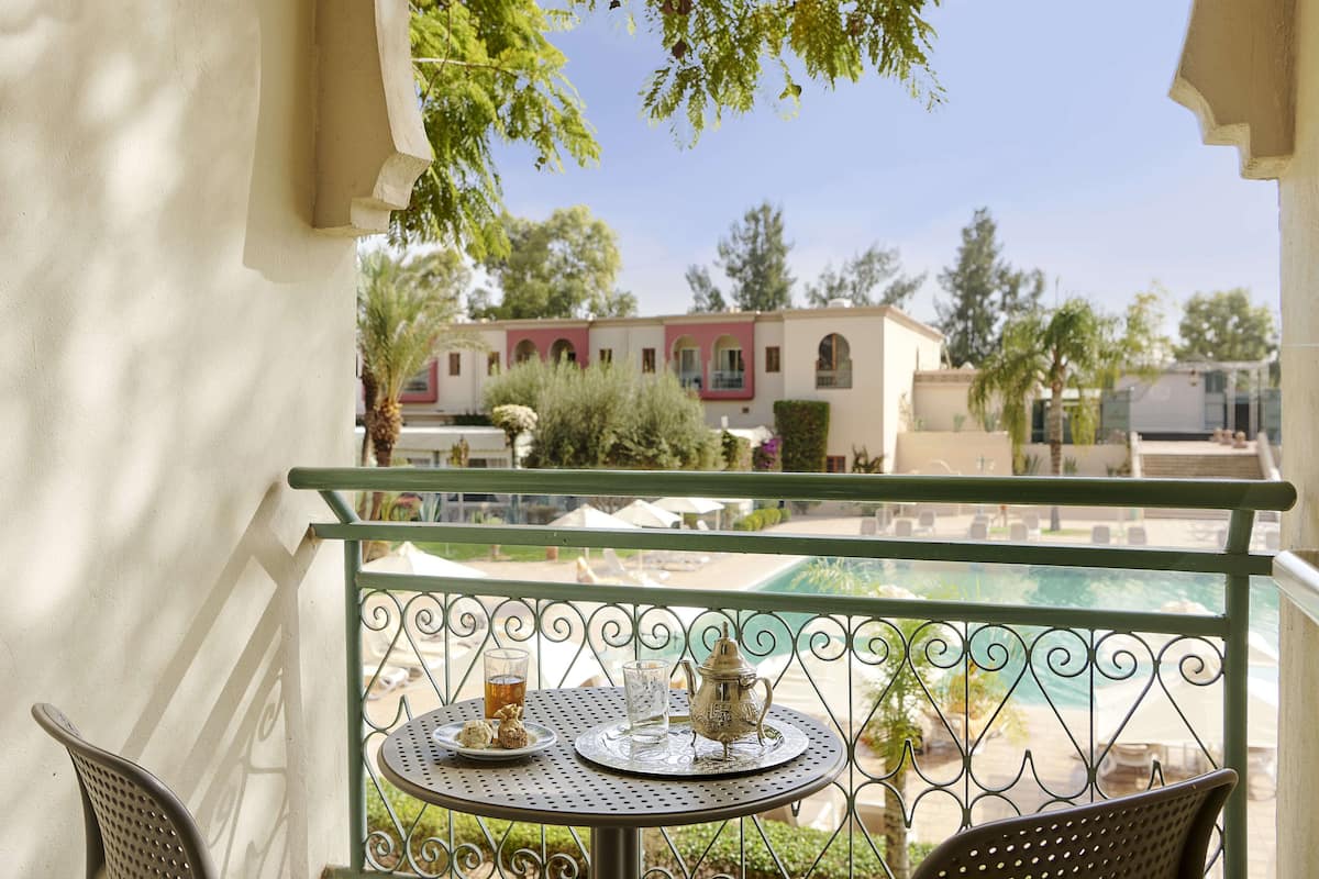 A balcony with a table set for two, a metal railing, and a view of a building and pool in the background.