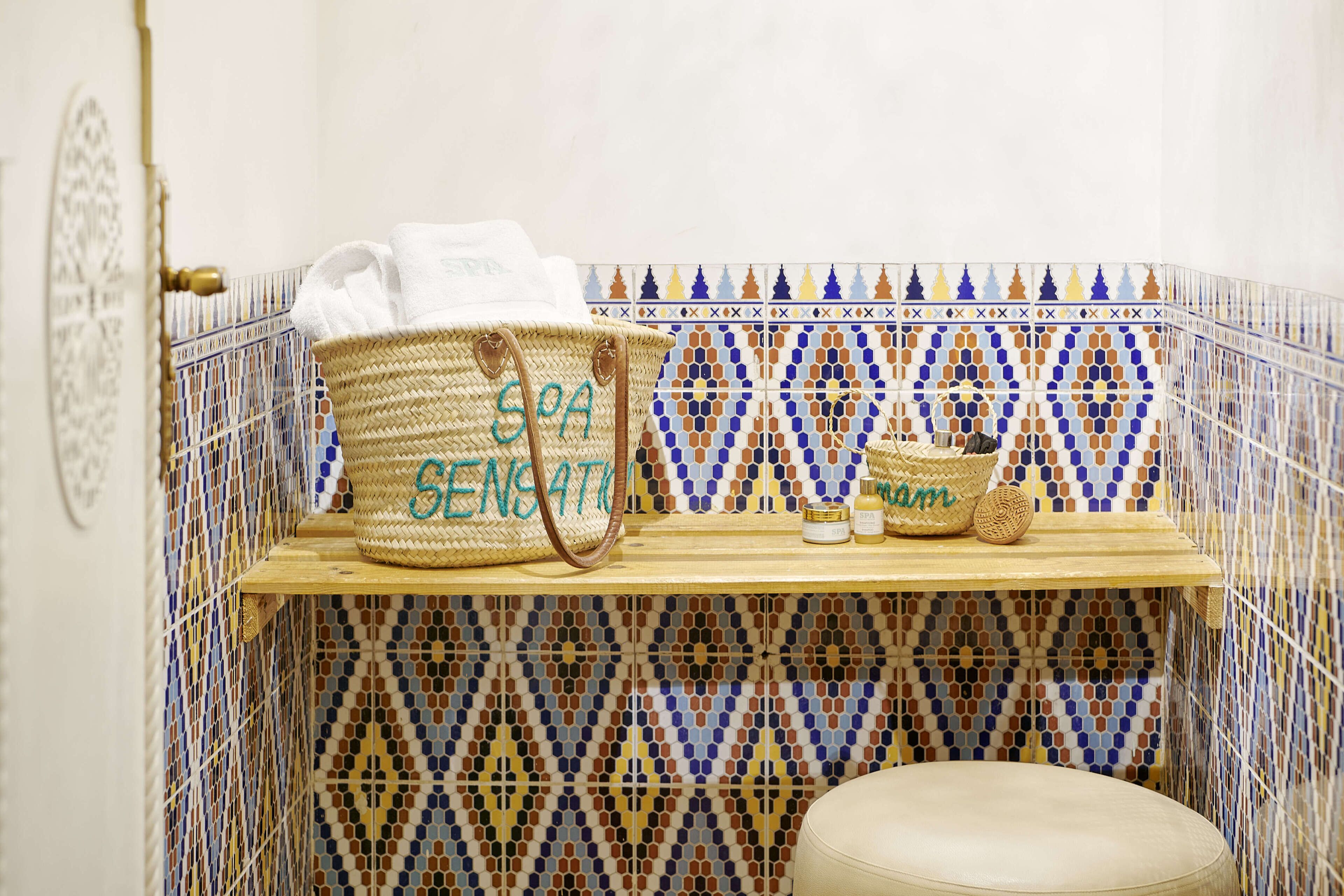 A bathroom with a tiled wall, a wooden shelf, and a woven basket labeled "SEA SENSATION."