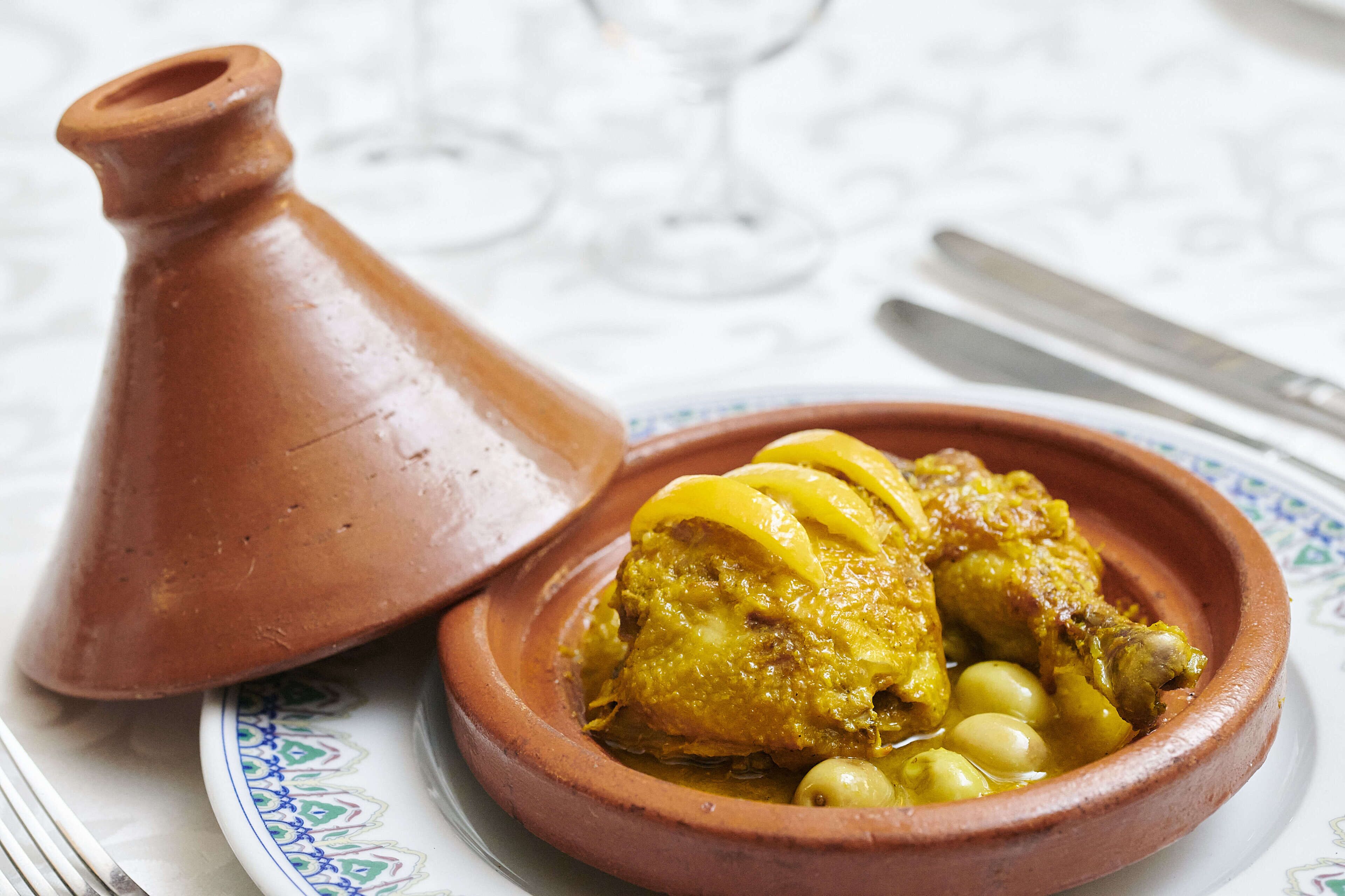 Un plat traditionnel marocain, un tajine aux olives, servi dans un pot en argile sur une assiette décorée.