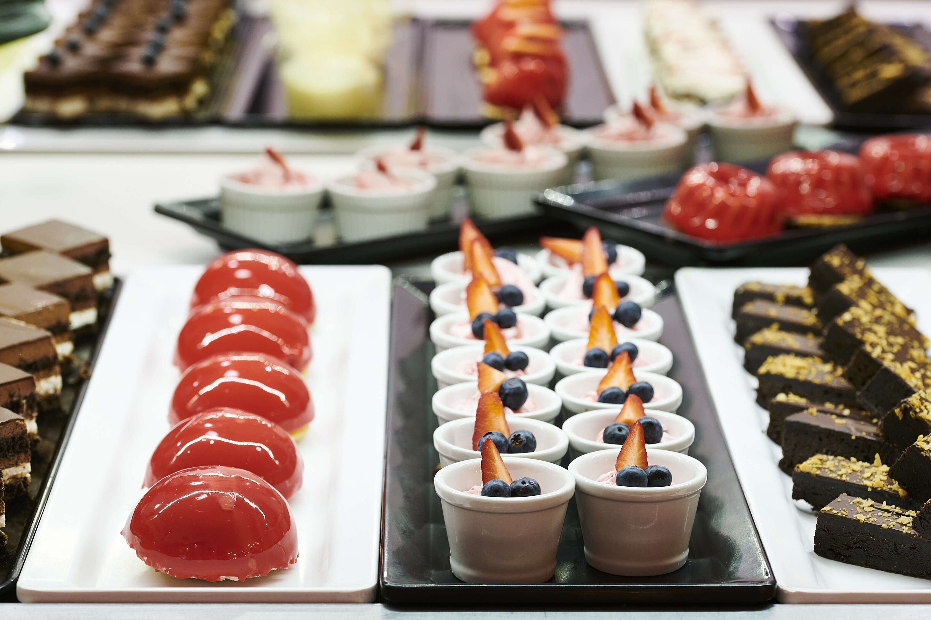 A variety of desserts arranged on trays, including red jelly desserts, small cups with blueberries and strawberries, and chocolate brownies.