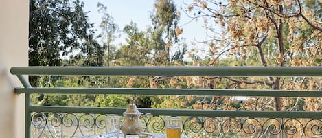 Varanda com mesa e duas cadeiras, com vista para um jardim com árvores e céu claro.